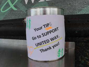 Bucket with sign reading "Your TIPS Go to Support United Way. Thank You!"