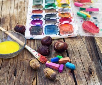 An photograph of a set of different paint colors and brush for painting on wooden background in the autumn style